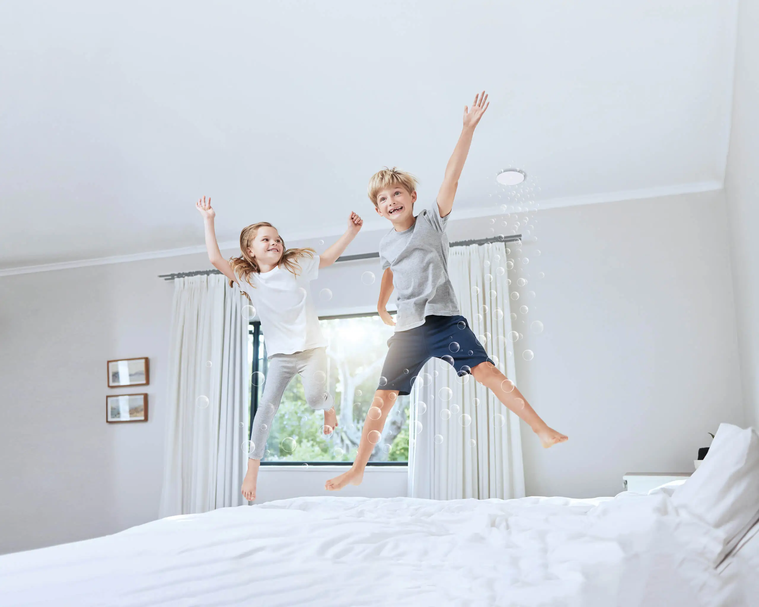 2 lachende kinderen springen op het bed in een kamer met verse lucht dankzij de zonale ventilatie en het ventiel in het plafond